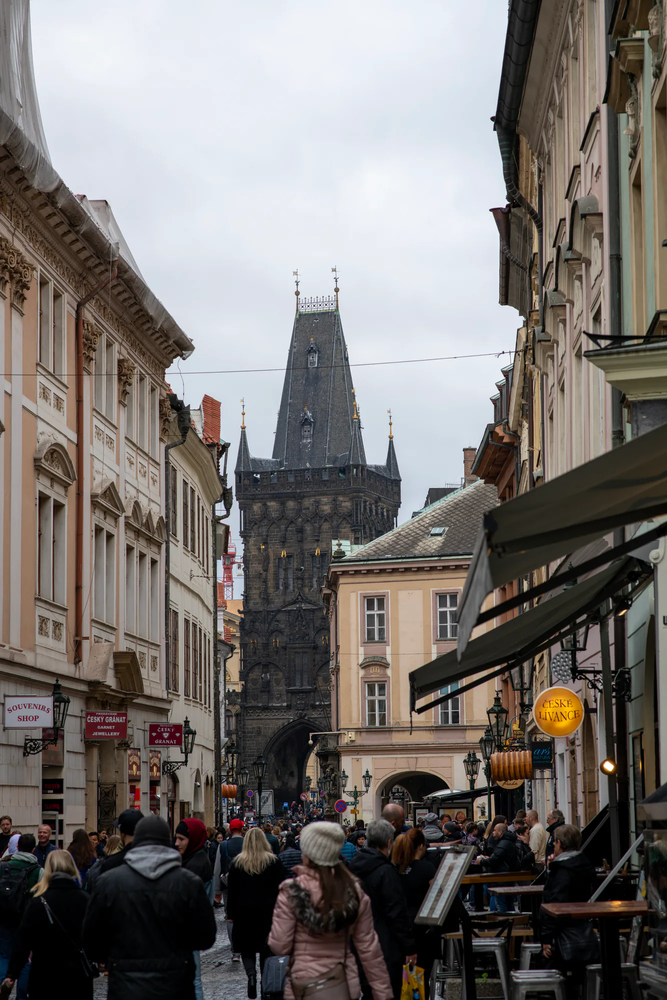 View along a historic Prague street after autumn rain, with the Old Town Hall tower rising between the façades.