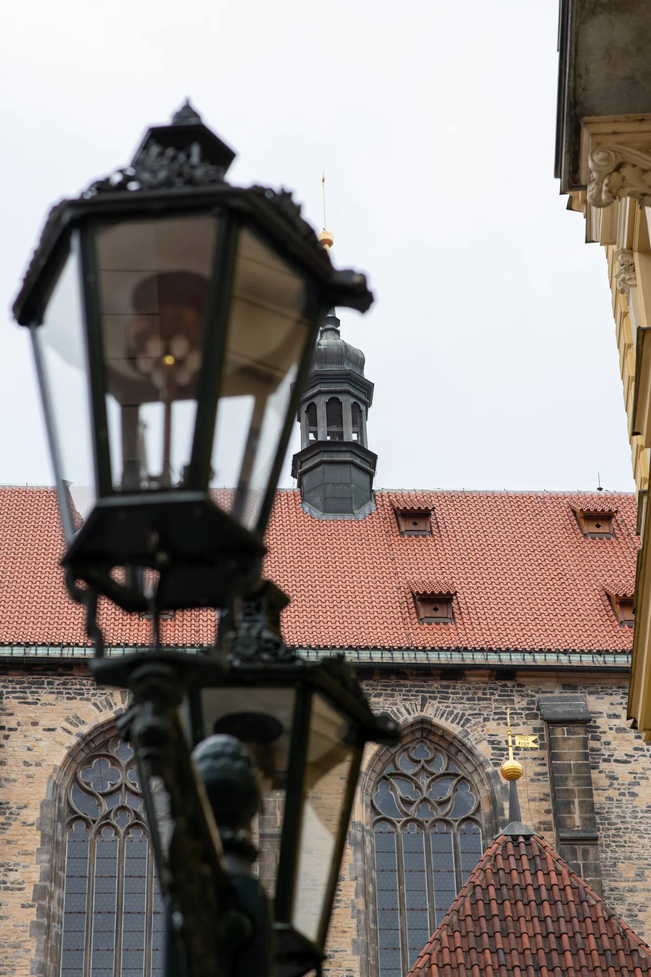 Old street lamps framing Gothic windows, red tiled roofs and historic architecture in Prague’s Old Town