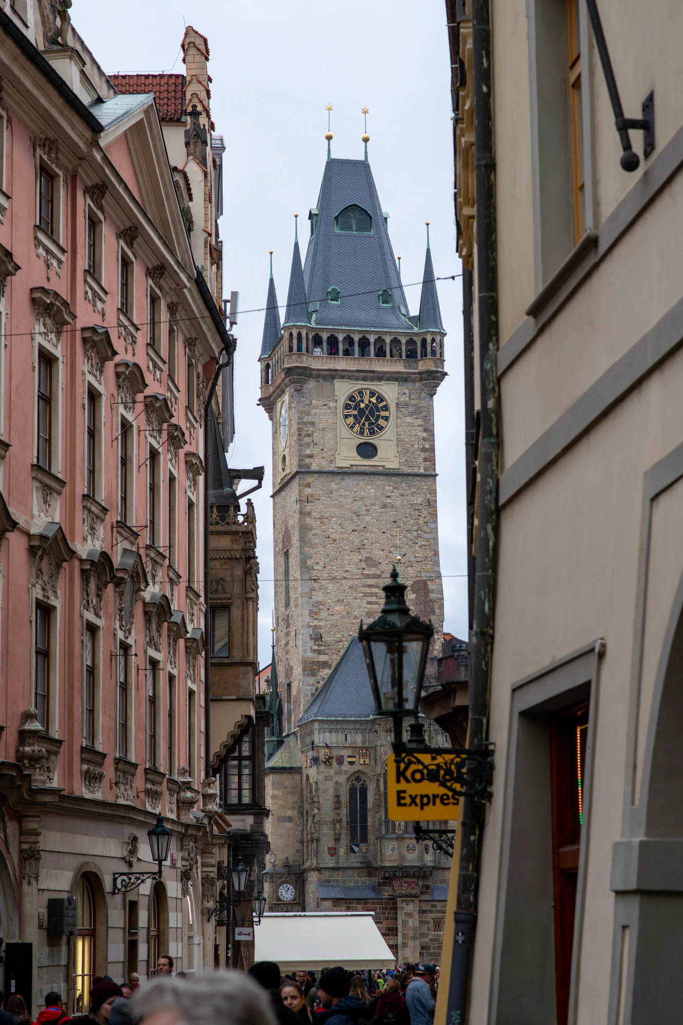 Old Town Hall tower framed by historic buildings along a crowded street in Prague.