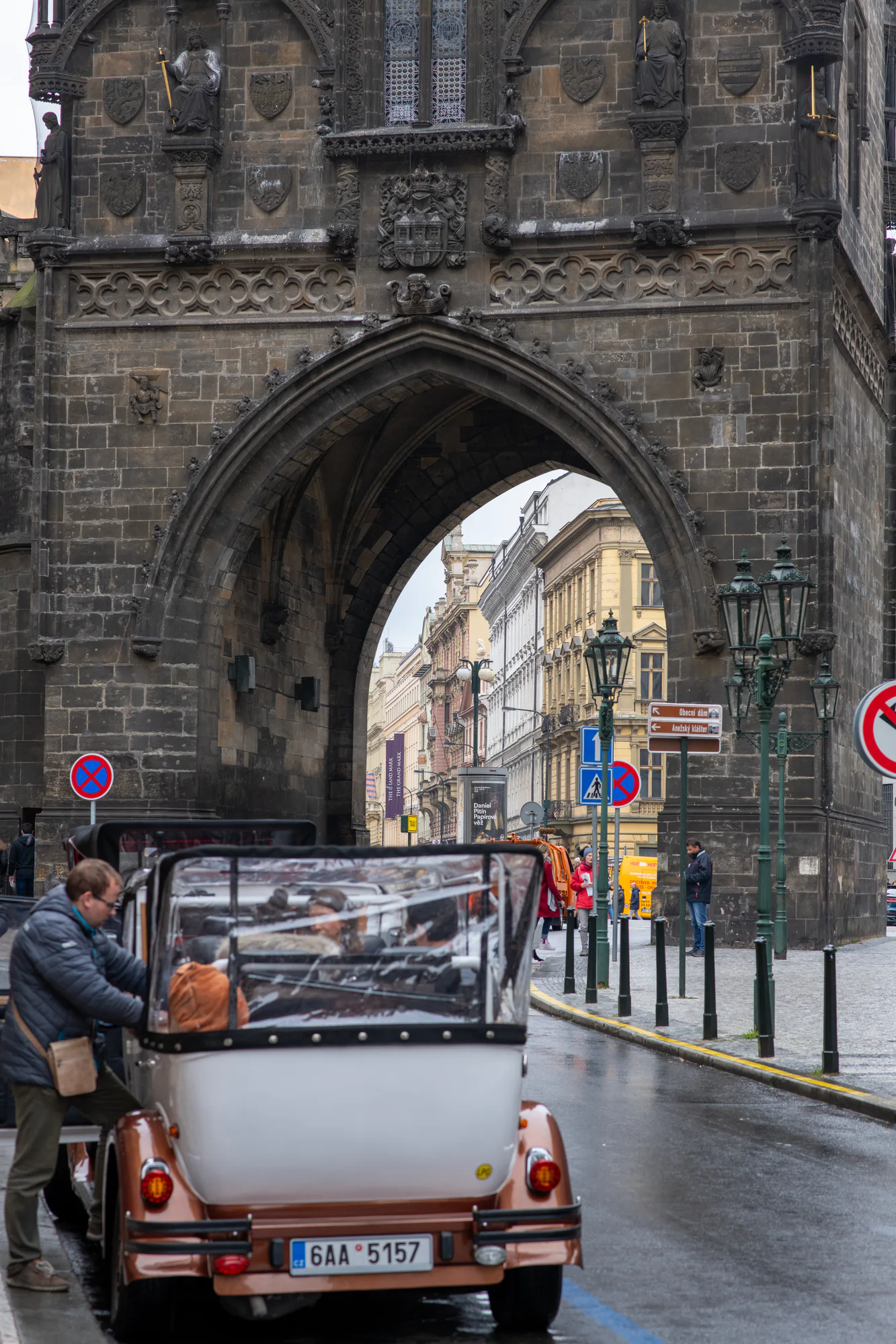 Powder Tower in Prague above a sightseeing car and pedestrians passing through the Gothic gateway.